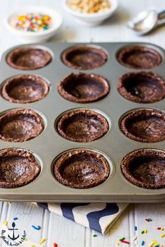 chocolate cupcakes in a muffin tin with sprinkles on the side