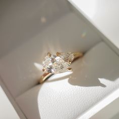 an engagement ring with two pear shaped diamonds on it's side in a white box