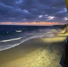 a beach with waves coming in to the shore and dark clouds over the water at sunset