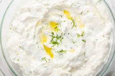 a glass bowl filled with white dip and topped with dill