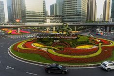 an intersection with cars and flowers in the center, surrounded by tall buildings on either side