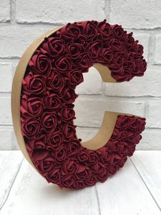 the letter c is made out of red paper flowers and has a wooden base,