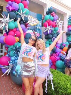 two women standing next to each other with their arms in the air and balloons behind them