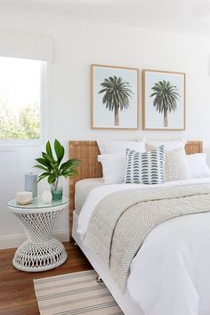 a bed with white sheets and pillows in a bedroom next to a table with two plants on it