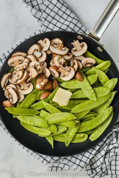 green beans, mushrooms and butter in a skillet on a marble counter top with a checkered towel