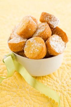 a bowl filled with powdered donuts sitting on top of a yellow table cloth