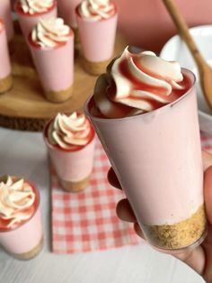 a person holding a cupcake in front of some desserts on a table with red and white checkered napkins