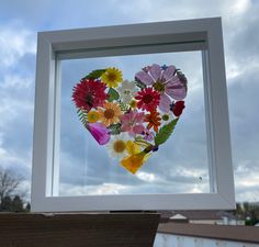 a heart made out of flowers in front of a window with blue sky and clouds