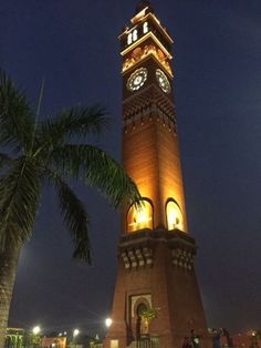 a clock tower lit up at night with palm trees in the foreground and people walking around