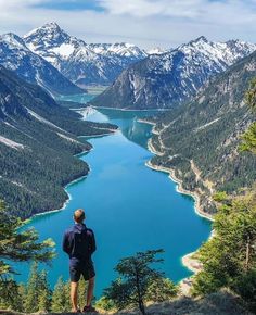 a man standing at the top of a mountain looking out over a lake and mountains