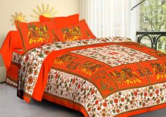 a bed with an orange comforter and two pillows on top of it in front of a window