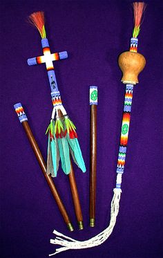 three different colored sticks with feathers on them next to a wooden cross and beaded crucifix