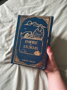 a woman's hand holding an empire storm book on top of a white sheet