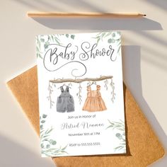 a baby shower card with two dresses hanging from a tree branch on top of it