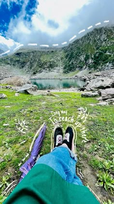 someone's feet are on the ground in front of a lake and mountain range