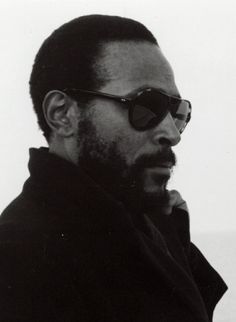 a man wearing sunglasses and a coat looks off into the distance