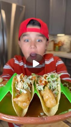 a young boy holding up two tacos in front of his face and making a funny face