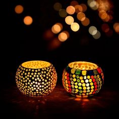 two colorful lit candles sitting on top of a table next to each other with lights in the background