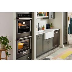 two ovens side by side in a kitchen with grey cabinets and white counter tops