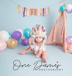 a baby wearing a crown sitting in front of balloons