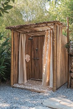 an outdoor toilet made out of straw and bamboo sticks with curtains on the doors, in front of some trees