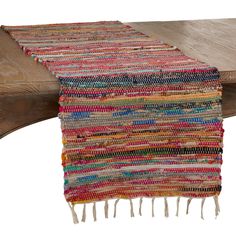 a multicolored table runner with tassels and fringe on it sitting on top of a wooden bench