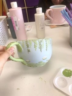 a person is painting a cup on a table with other items in the room behind them