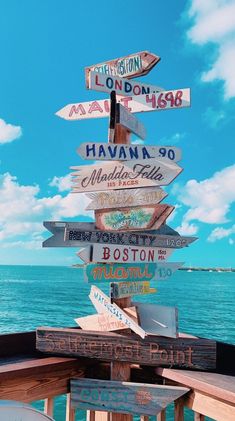 a wooden sign post with many different signs on it's side near the ocean