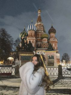 a woman wearing a fur coat in front of a building with domes on it at night