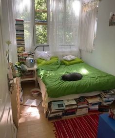 a bed with green sheets and pillows in a room filled with books, magazines and other items