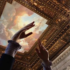 two hands reaching up into the sky above a ceiling with gold and white designs on it