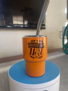 an orange cup with a straw sticking out of it sitting on top of a blue stand