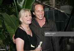 a man and woman standing next to each other in front of some green plants, smiling at the camera