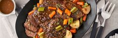 a black plate topped with meat and veggies on top of a white table