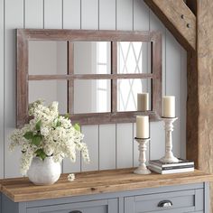 a vase with white flowers and candles on a table in front of a wall mirror