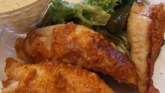 two pieces of fried chicken on a white plate with salad and dressing in a glass container