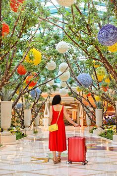 a woman in a red dress is holding a suitcase and looking at the ceiling with colorful balls