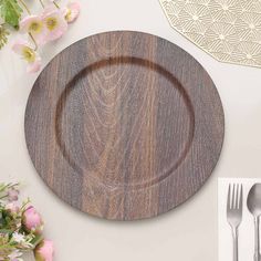 a wooden plate sitting on top of a white table next to silverware and flowers