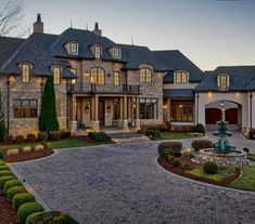 a large house with a fountain in the front yard and landscaping around it at dusk