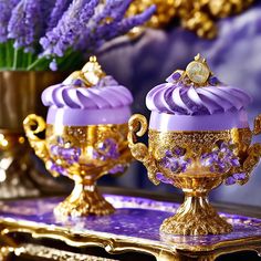 two purple and gold cupcakes sitting on top of a table next to a vase filled with flowers