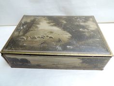 an old tin box with sheep grazing on the grass and trees painted on it's sides