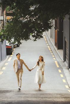 a man and woman holding hands while walking down the street