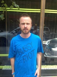 a man standing in front of a building with his hand on his hip and wearing a blue shirt that says boss riot