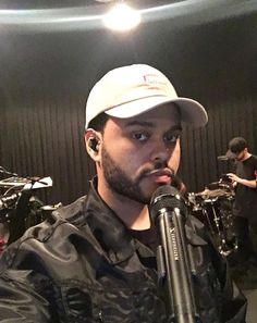 a man holding a microphone in front of him and looking at the camera while wearing a white hat