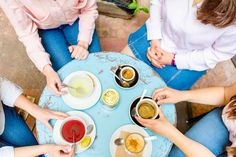 four people sitting around a table with cups of tea and saucers on it, all holding spoons in their hands