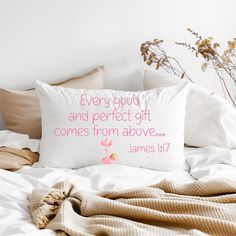 a white pillow with pink lettering sitting on top of a bed next to pillows and blankets