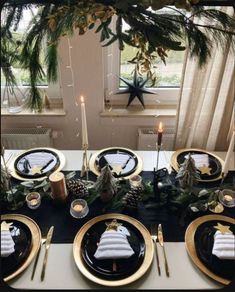 the table is set with black and gold plates, silverware, pine cones, greenery, candlesticks