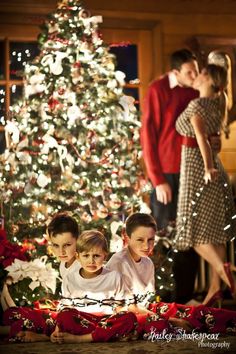 three children sitting in front of a christmas tree