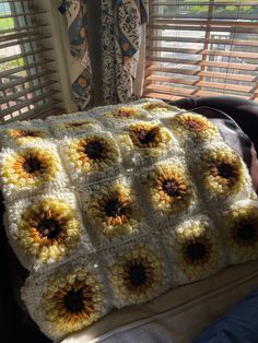 a crocheted sunflower blanket sitting on top of a couch next to a window