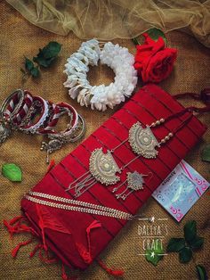 red saree and jewelry laid out on a cloth with flowers in the middle, along with other accessories